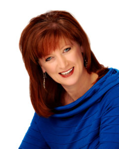 A woman with red hair and blue shirt smiling.