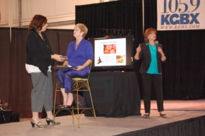Three women are standing on stage and one is holding a microphone.