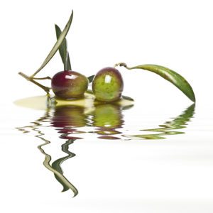 Green olives with leaves covered in olive oil and reflected on water.